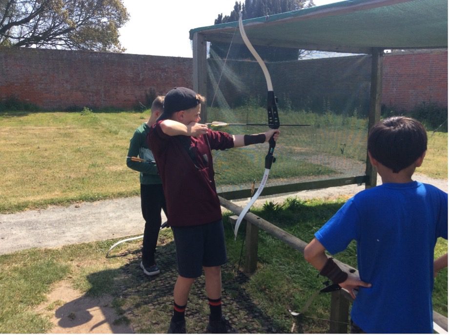 boy shoots a bow and arrow while two other boys watch him